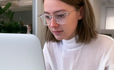 Frau in weißem Pullover arbeitet konzentriert am Laptop und trägt eine Brille mit klaren Gläsern