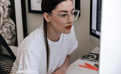 Frau arbeitet im Homeoffice am Desktop-Rechner und trägt eine Brille mit klaren Gläsern