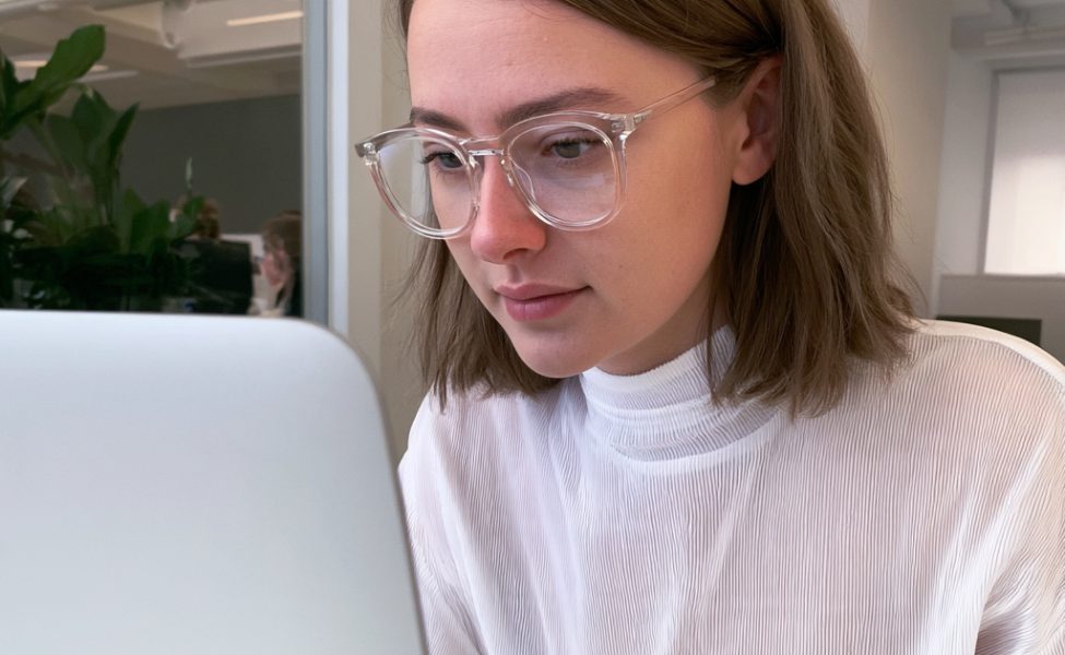 Frau in weißem Pullover arbeitet konzentriert am Laptop und trägt eine Brille mit klaren Gläsern