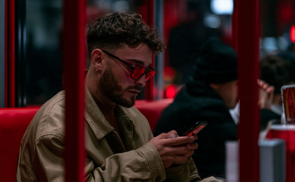 Mann mit roter Brille am Smartphone in einem Zimmer mit buntem Neonlicht am Abend